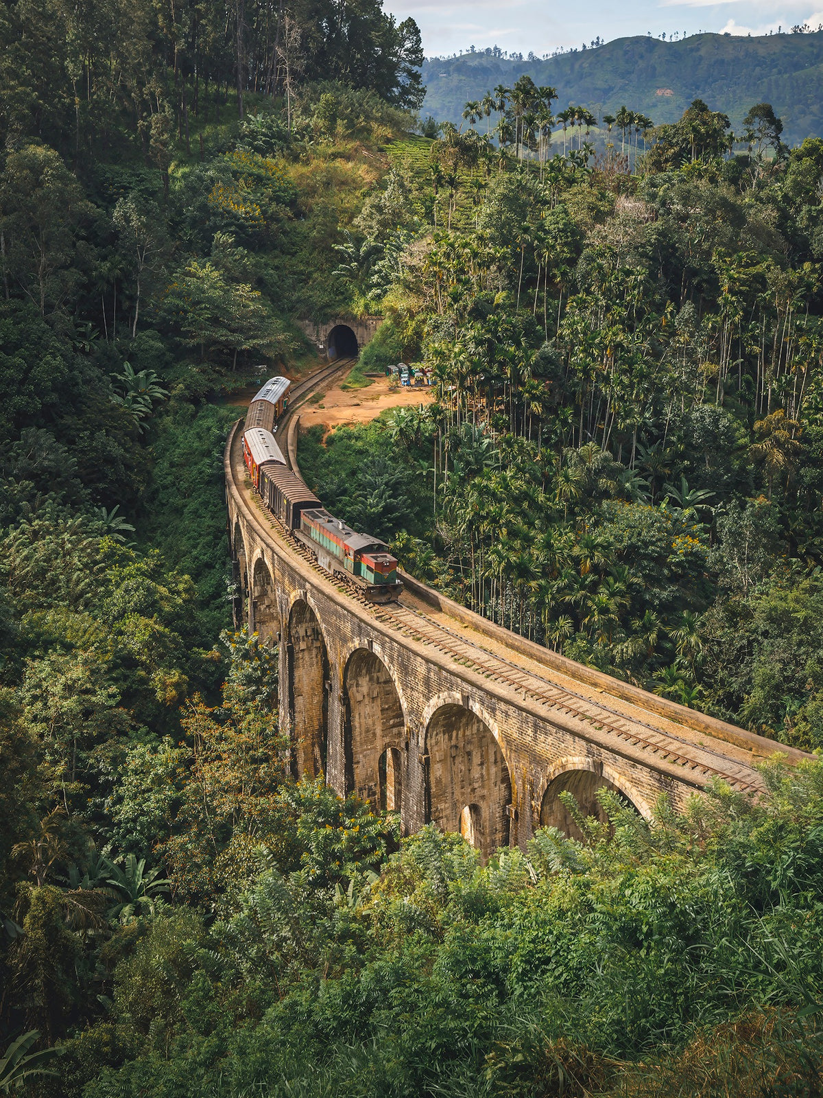 Train crossing the Nine Arches Bridge in Ella, Sri Lanka, surrounded by lush tropical vegetation.